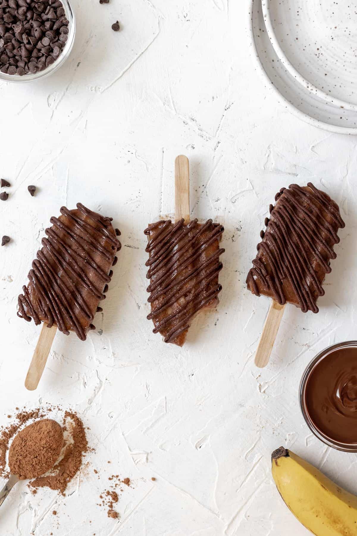 3 chocolate popsicles lined up on a white background with a bite taken out of the middle one.