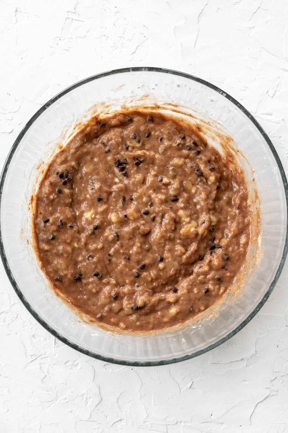 Mashed bananas mixed with chocolate chips and the rest of the ingredients in a glass bowl.