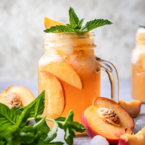 Bourbon peach smash garnished with fresh mint in a mason jar.