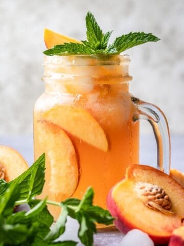 Bourbon peach smash garnished with fresh mint in a mason jar.