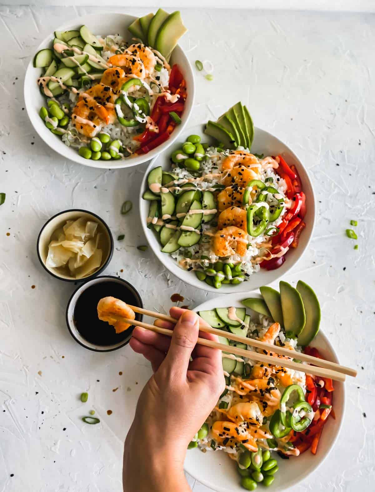 Shrimp Poke Bowls and a hand holding chopsticks with a piece of shrimp dunked in soy sauce