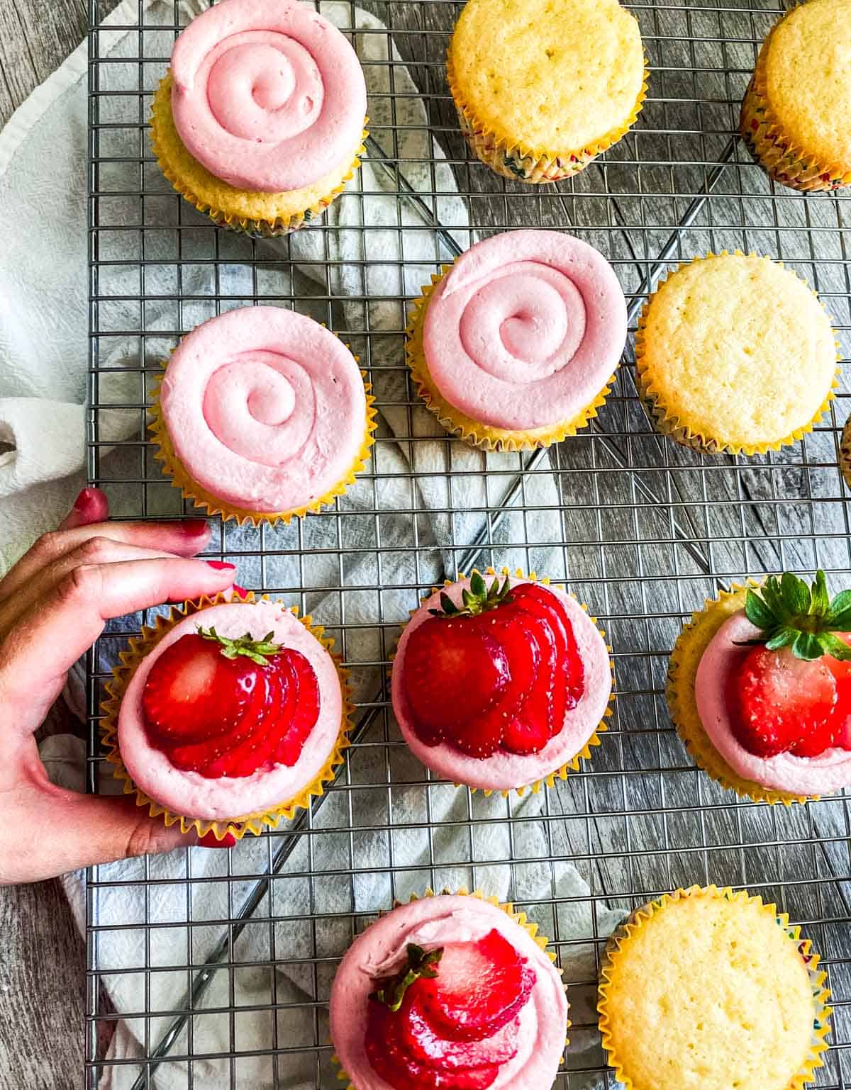 almond cupcakes with strawberry buttercream frosting on a cooling rack