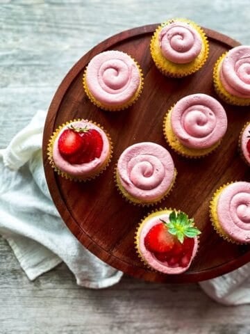 Almond cupcakes with strawberry frosting on a wooden cake stand