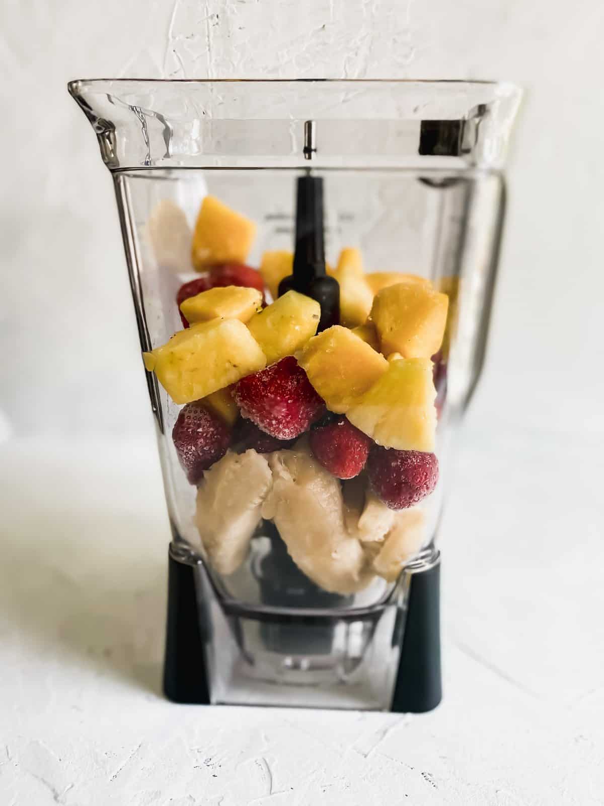frozen strawberries and pineapples in a blender with fresh bananas