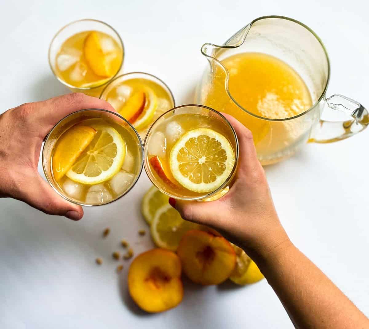 Two hands "cheersing" peach lemonade in cups 