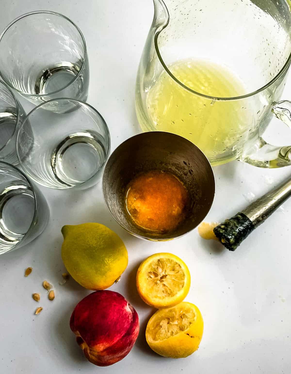 Muddled peaches in a cocktail shaker and lemon juice in a pitcher