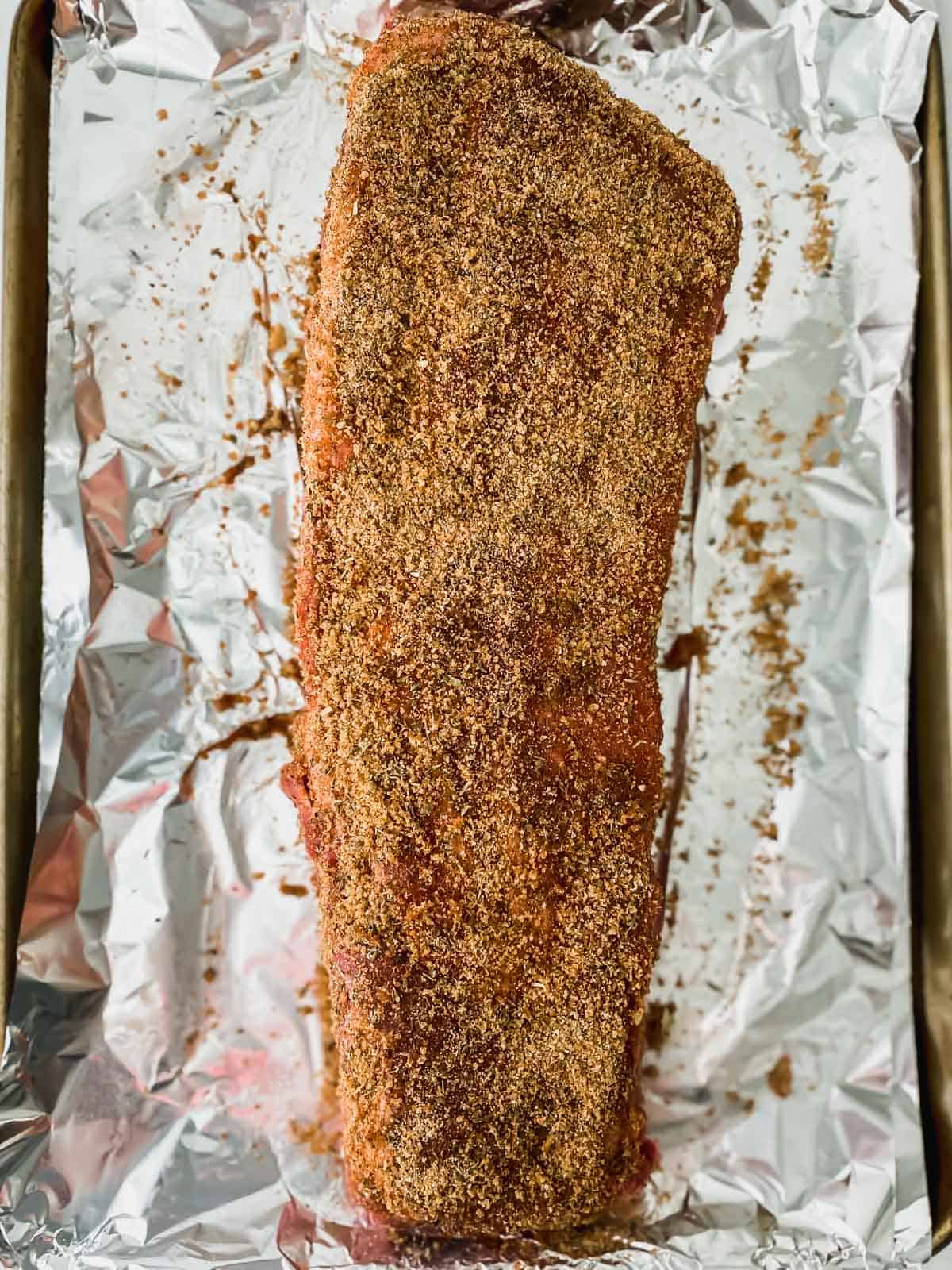slab of ribs with dry rub on it on top of an aluminum foil covered sheet pan