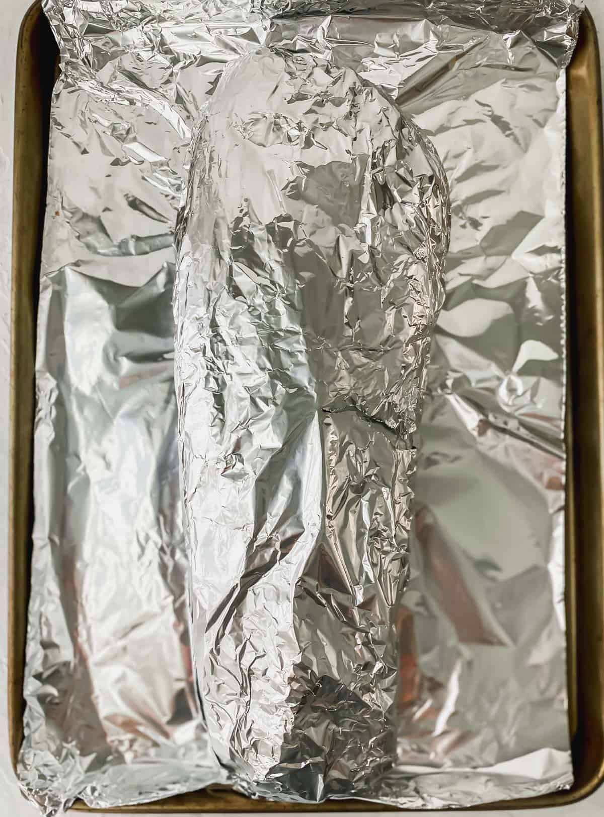 aluminum foil covered sheet pan with an aluminum foil wrapped slab of ribs on top