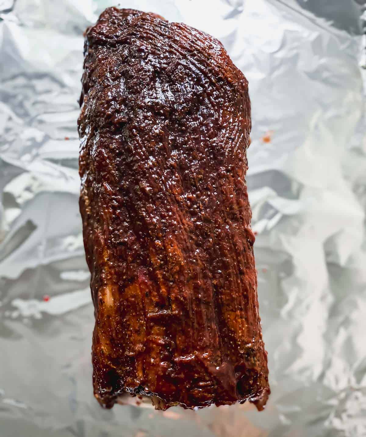 slab of ribs on an aluminum foil covered sheet pan with bbq sauce brushed on top