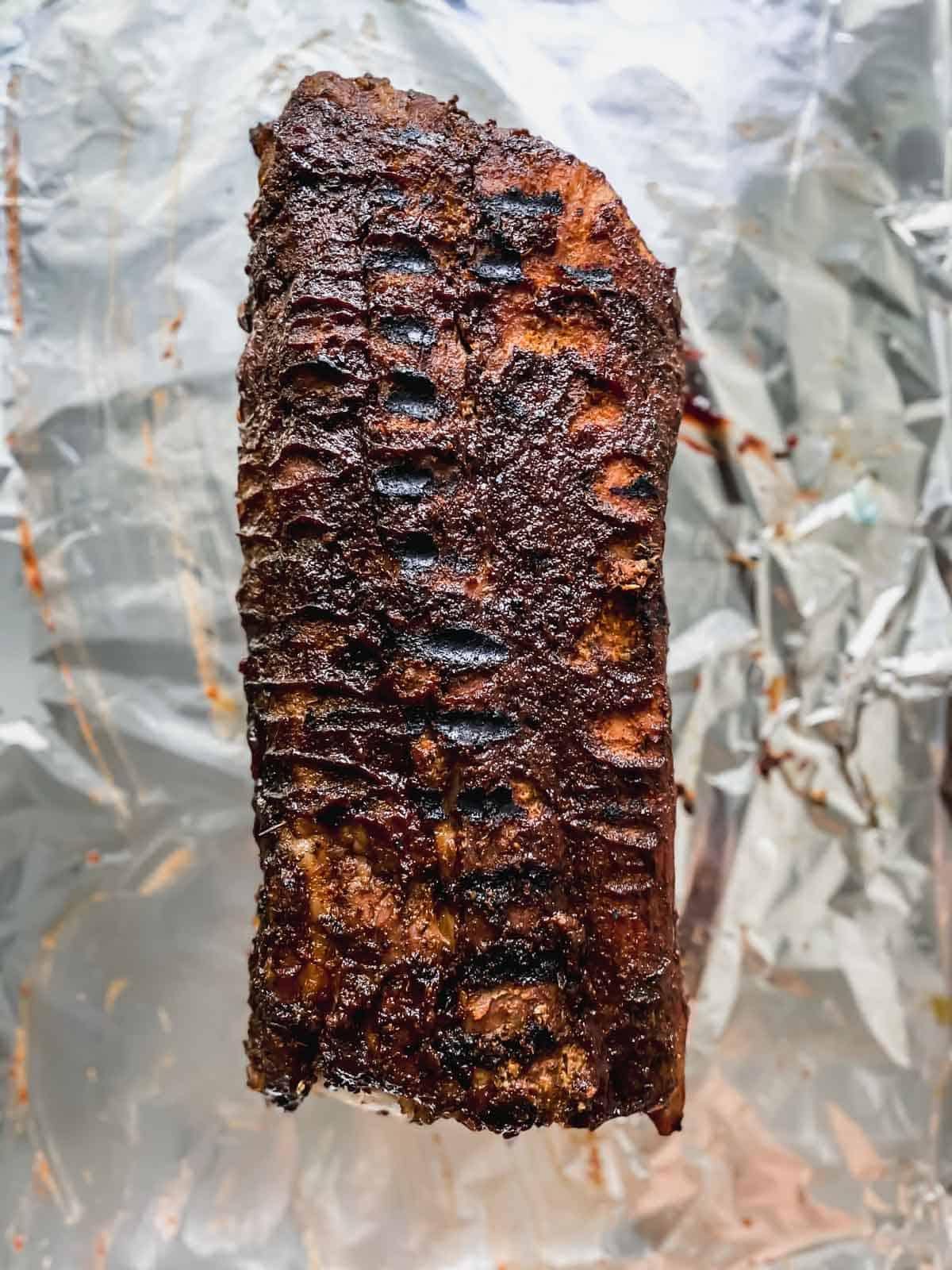 grilled slab of ribs on a sheet pan covered with aluminum foil