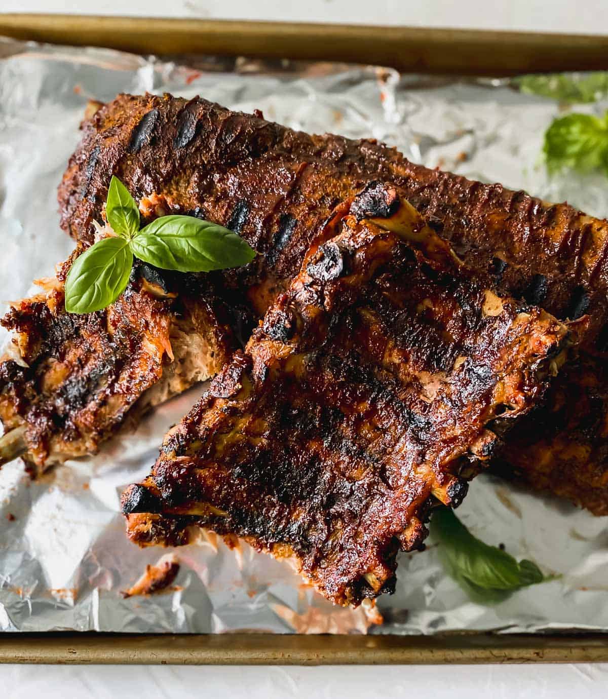 bbq ribs with basil on a sheet pan covered in aluminum foil