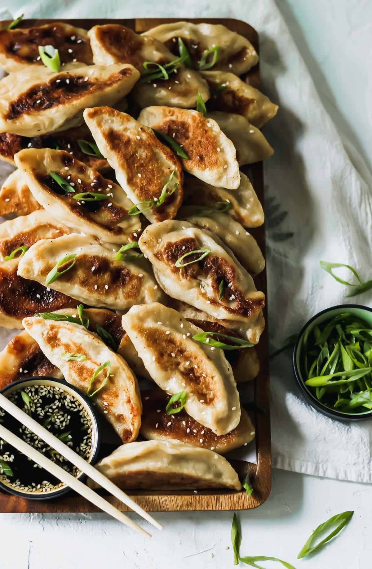 Chinese chicken dumplings with sesame soy sauce, chopsticks, and a bowl of scallions.