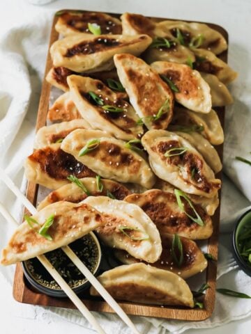 Chicken Dumplings on a wooden tray with chopsticks, scallions, and sesame soy dippings sauce.