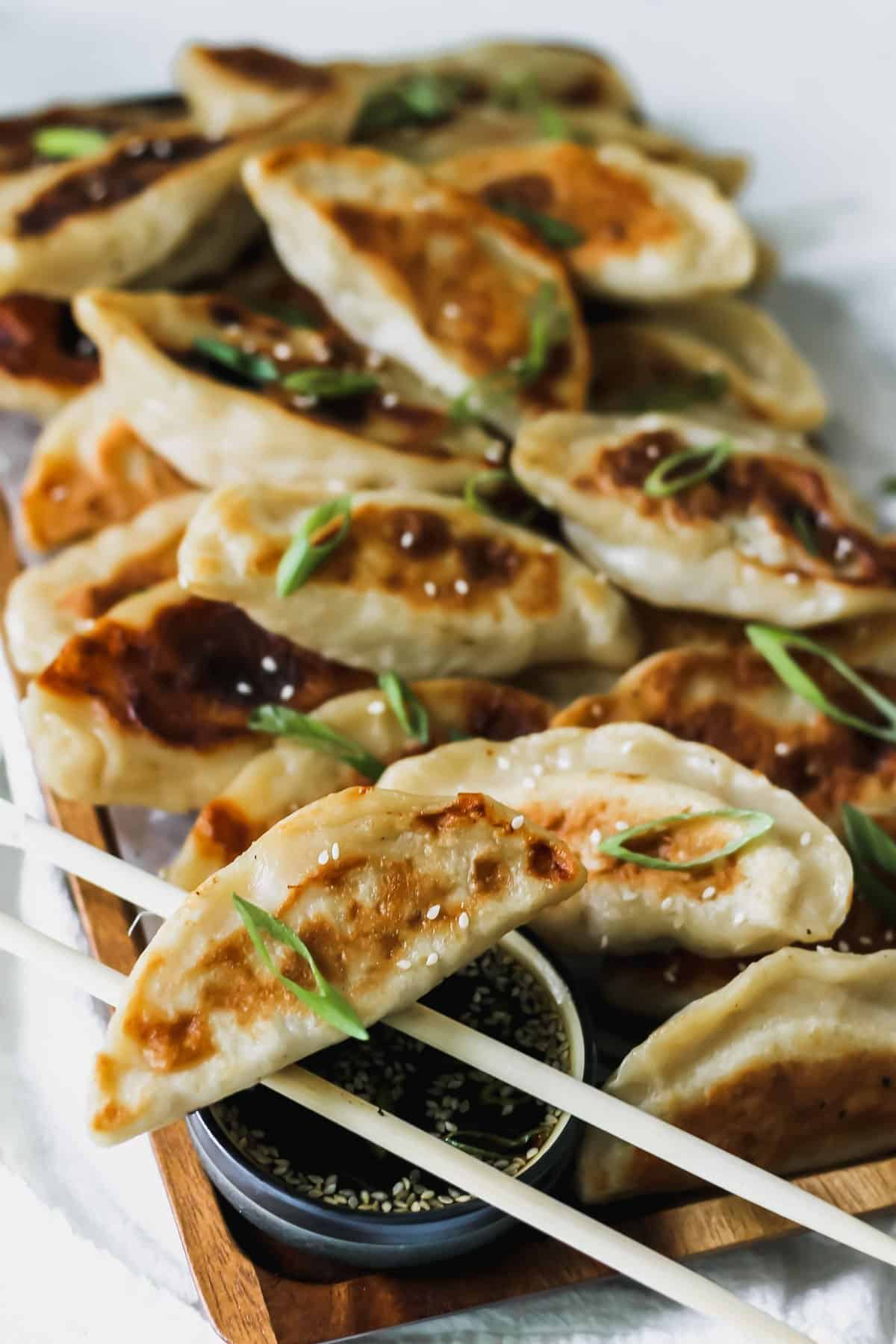 Chinese chicken dumplings with sesame soy sauce on a wooden tray with a white napkin behind it.