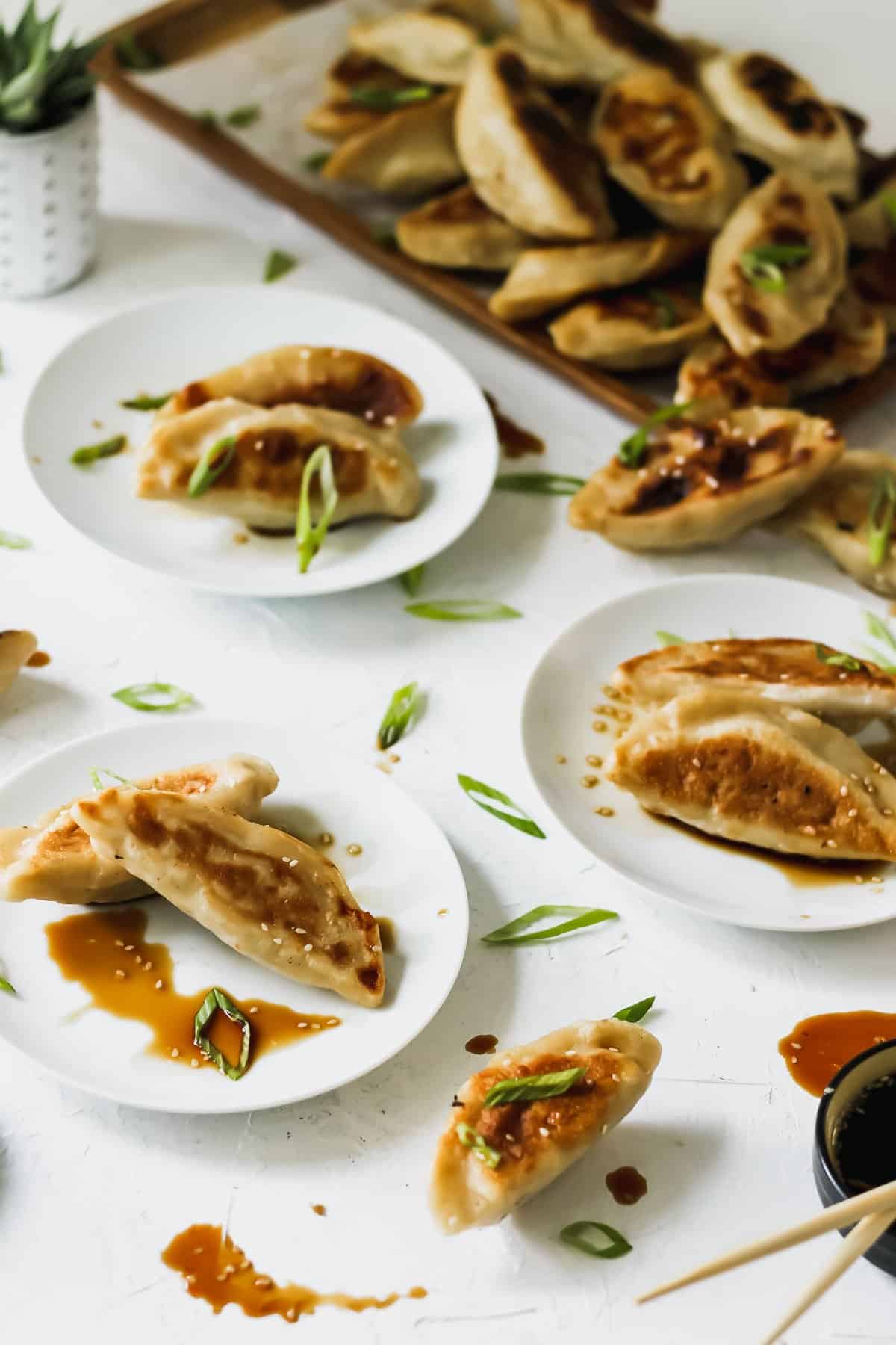 Chicken dumplings on white plates with a mess of dipping sauce and scallions.