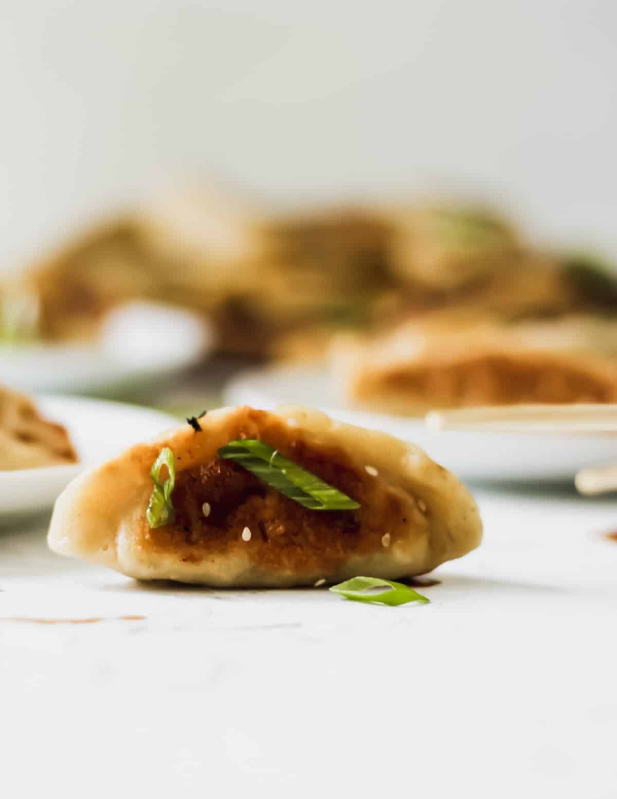 A chinese chicken dumpling with scallions on top.