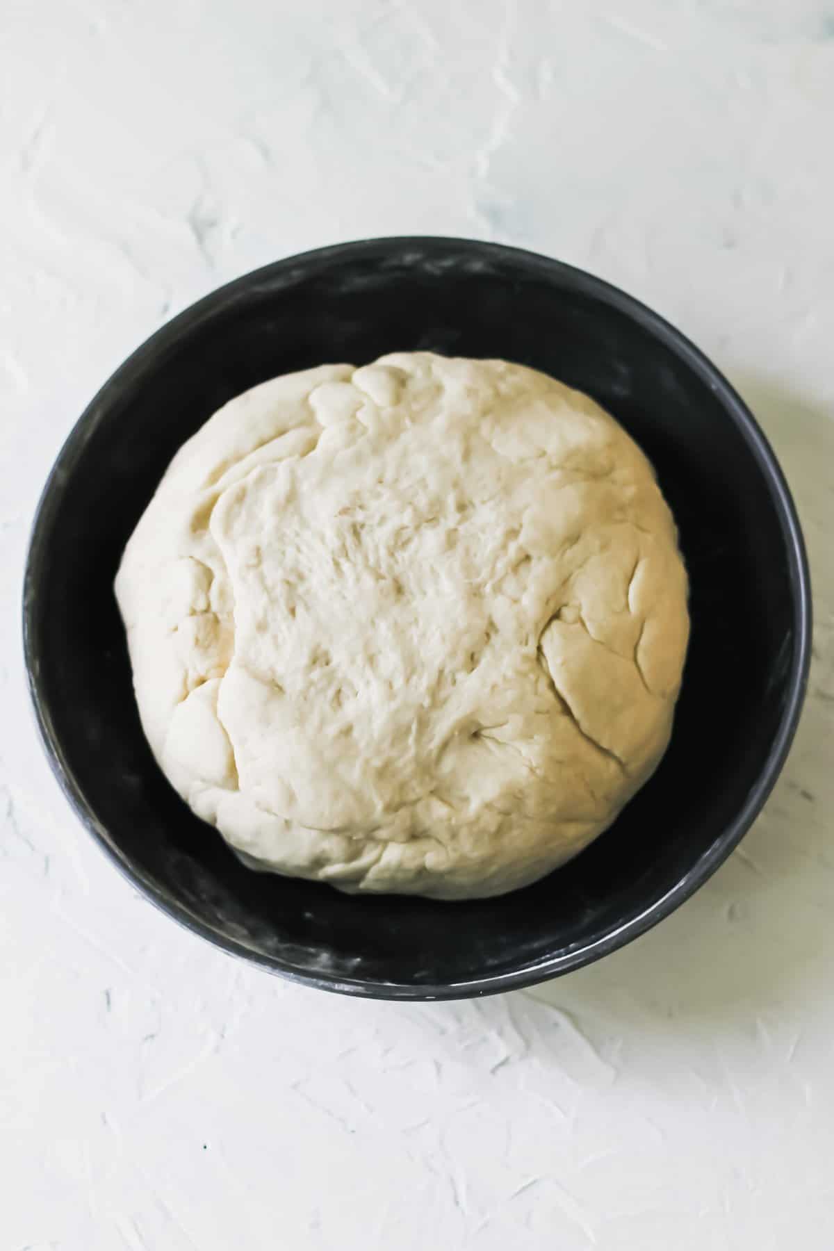 A ball of dumpling dough in a black bowl.