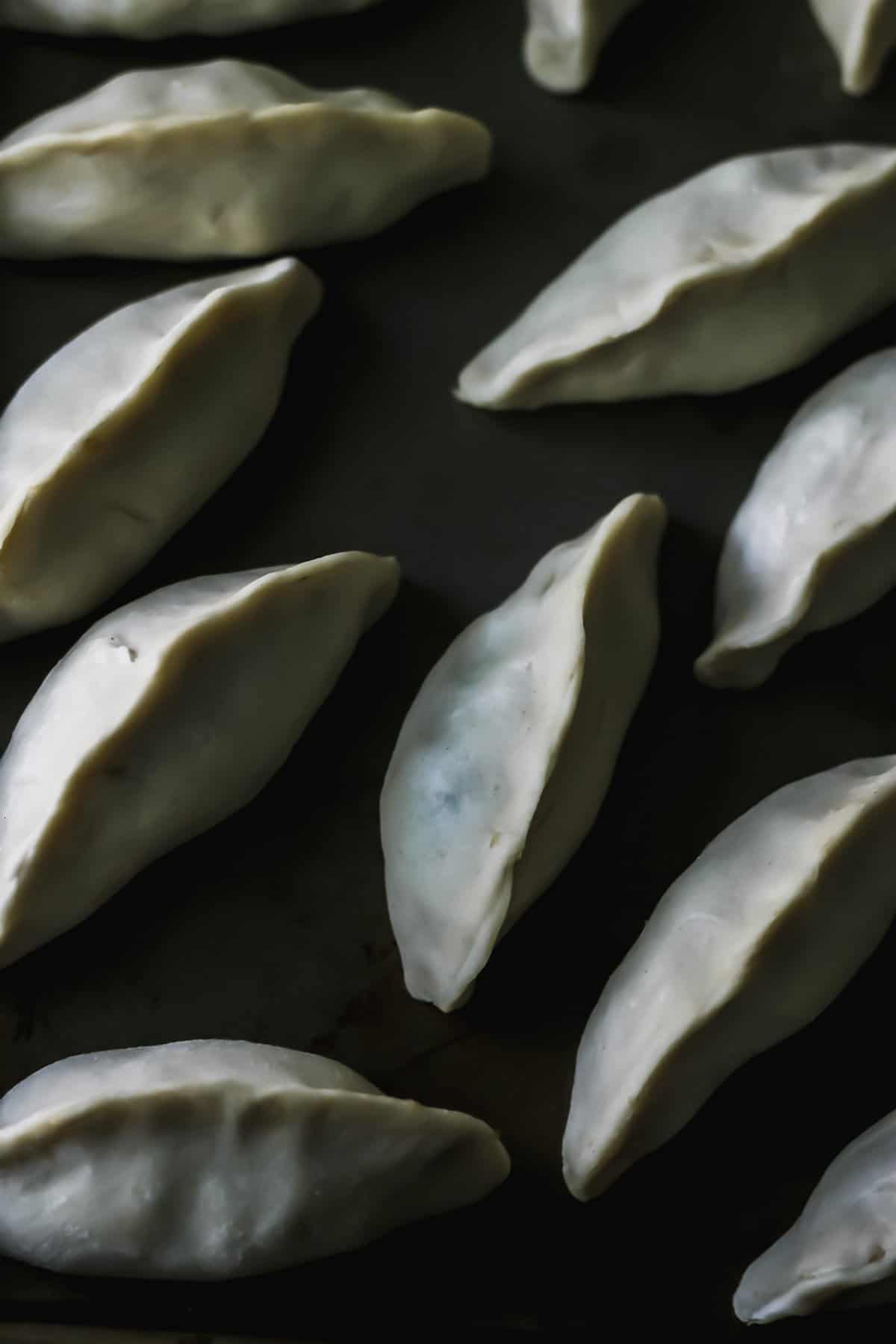 Raw folded chicken dumplings on a cookie sheet, ready for cooking.