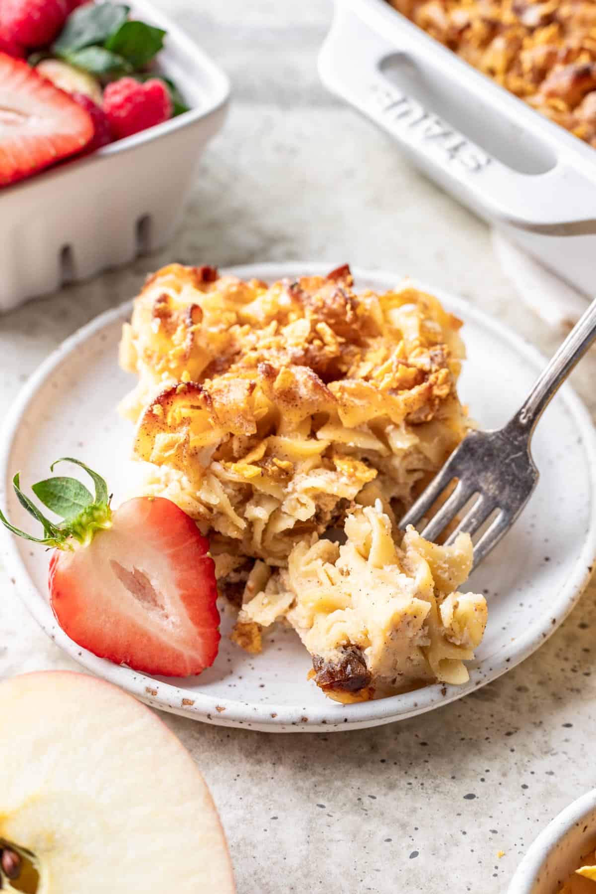 A piece of noodle kugel on a white plate with a fork.