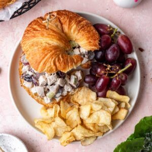 Cranberry pecan chicken salad on a croissant with a side of grapes and potato chips.