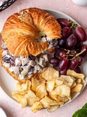 Cranberry pecan chicken salad on a croissant with a side of grapes and potato chips.