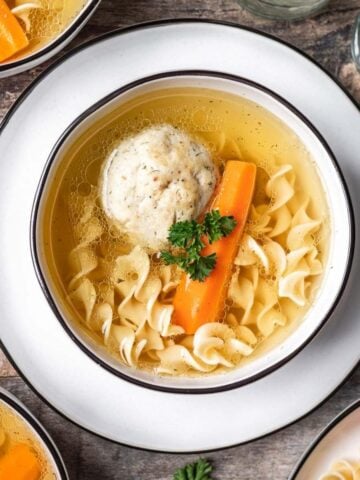 Instant pot matzo ball soup in a white bowl with a matzo ball, carrot, and egg noodles.