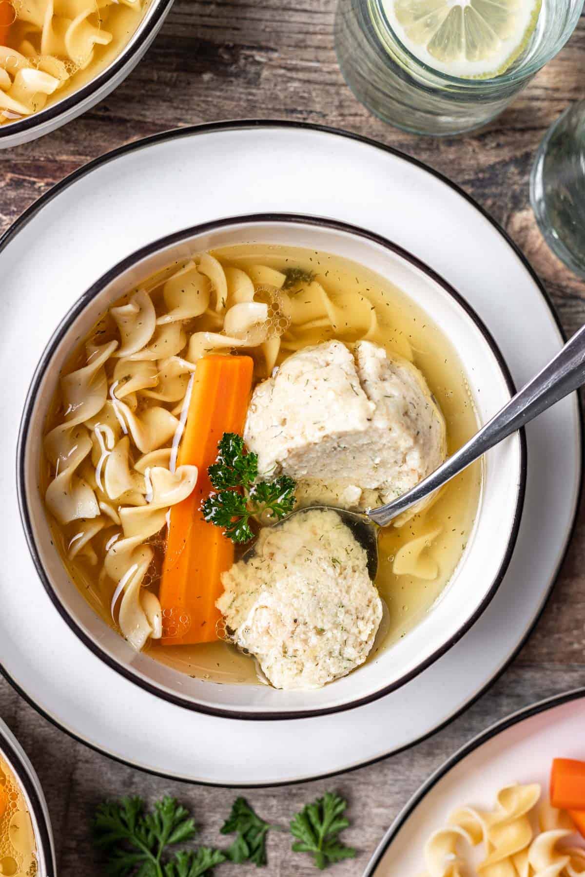Instant pot matzo ball soup in a white bowl with the matzo bowl split in half with a spoon.