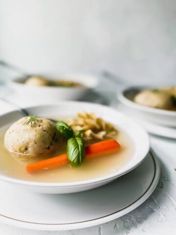 matzo ball soup in a white bowl on top of a white plate