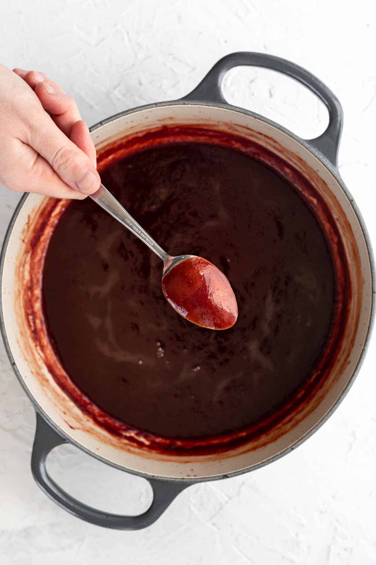 Thick barbecue sauce in a sauce pan with a spoon coated in sauce above it.