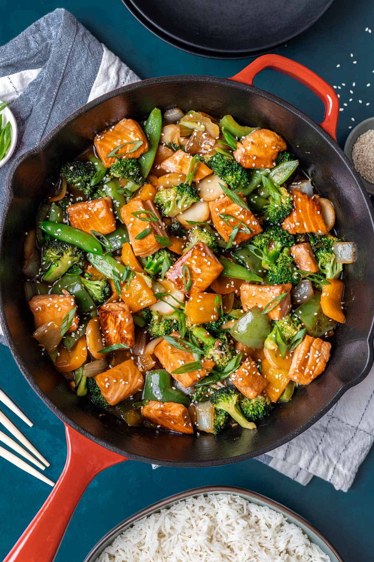 Teriyaki salmon stir fry garnished with green onions and sesame seeds in a large skillet.