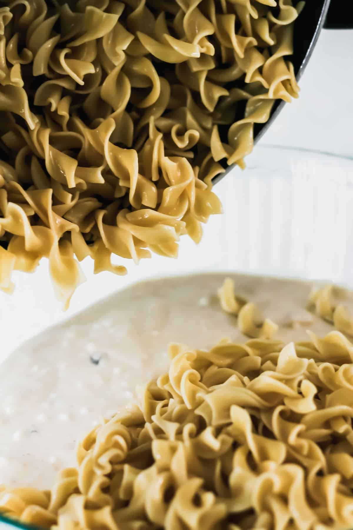 Dumping cooked egg noodles into the liquid mixture.