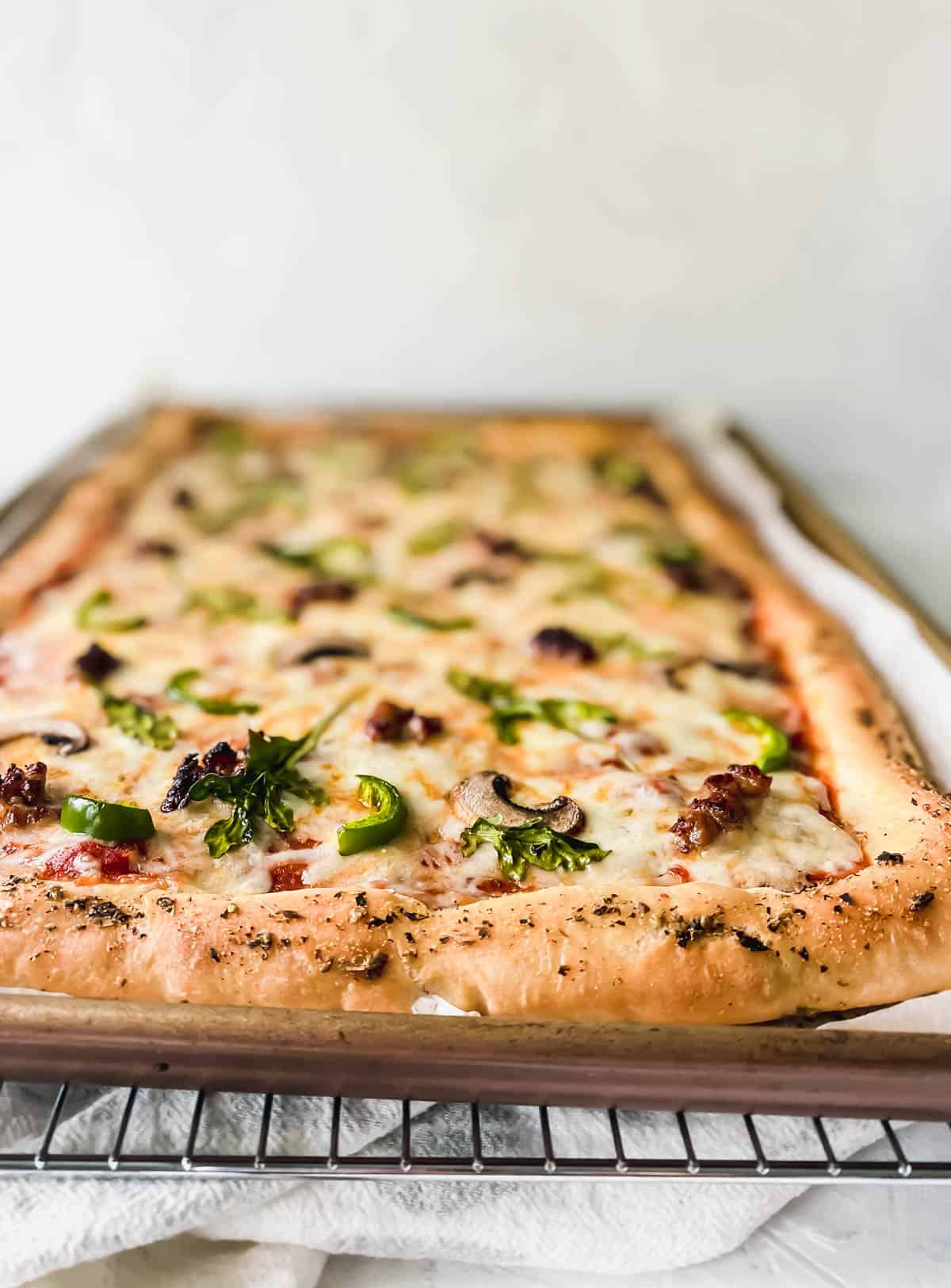 mushroom, sausage, and arugula pizza on a sheet pan on top of a cooling rack