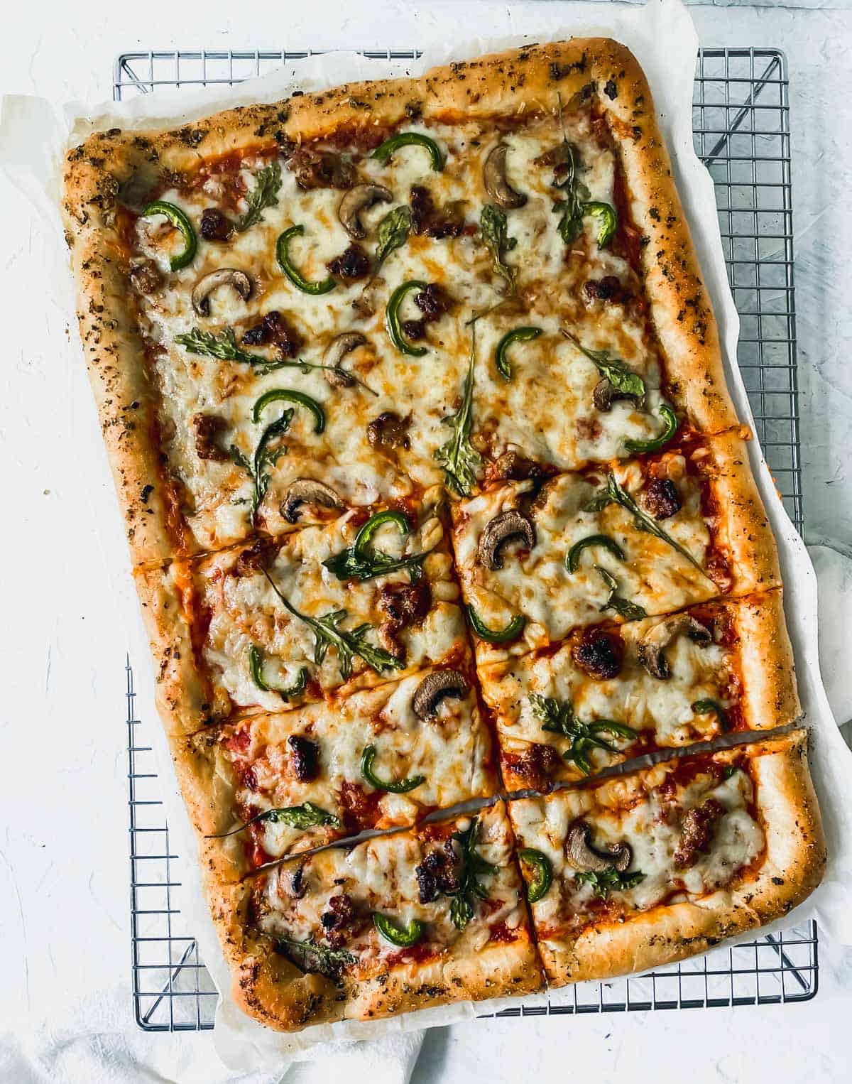 cooked mushroom, sausage, and arugula pizza on a cooling rack