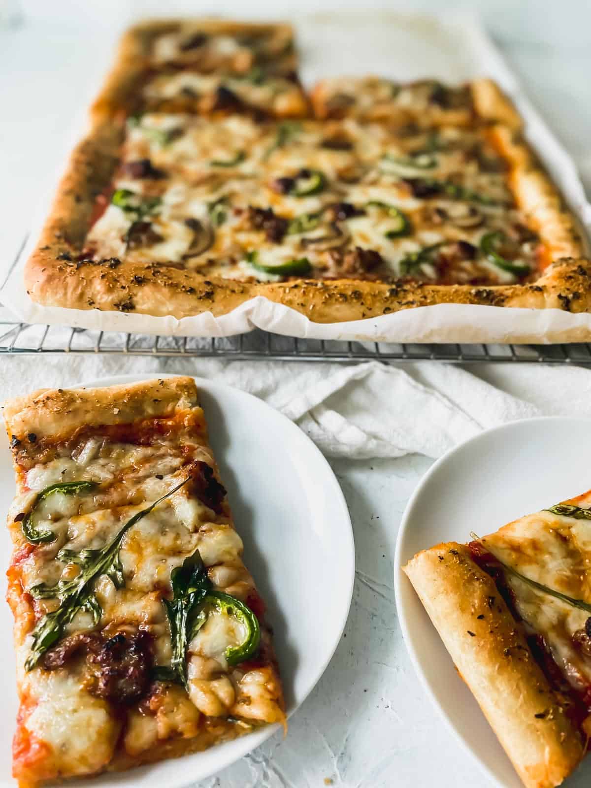 pizza on a cooling rack with two slices on small white plates