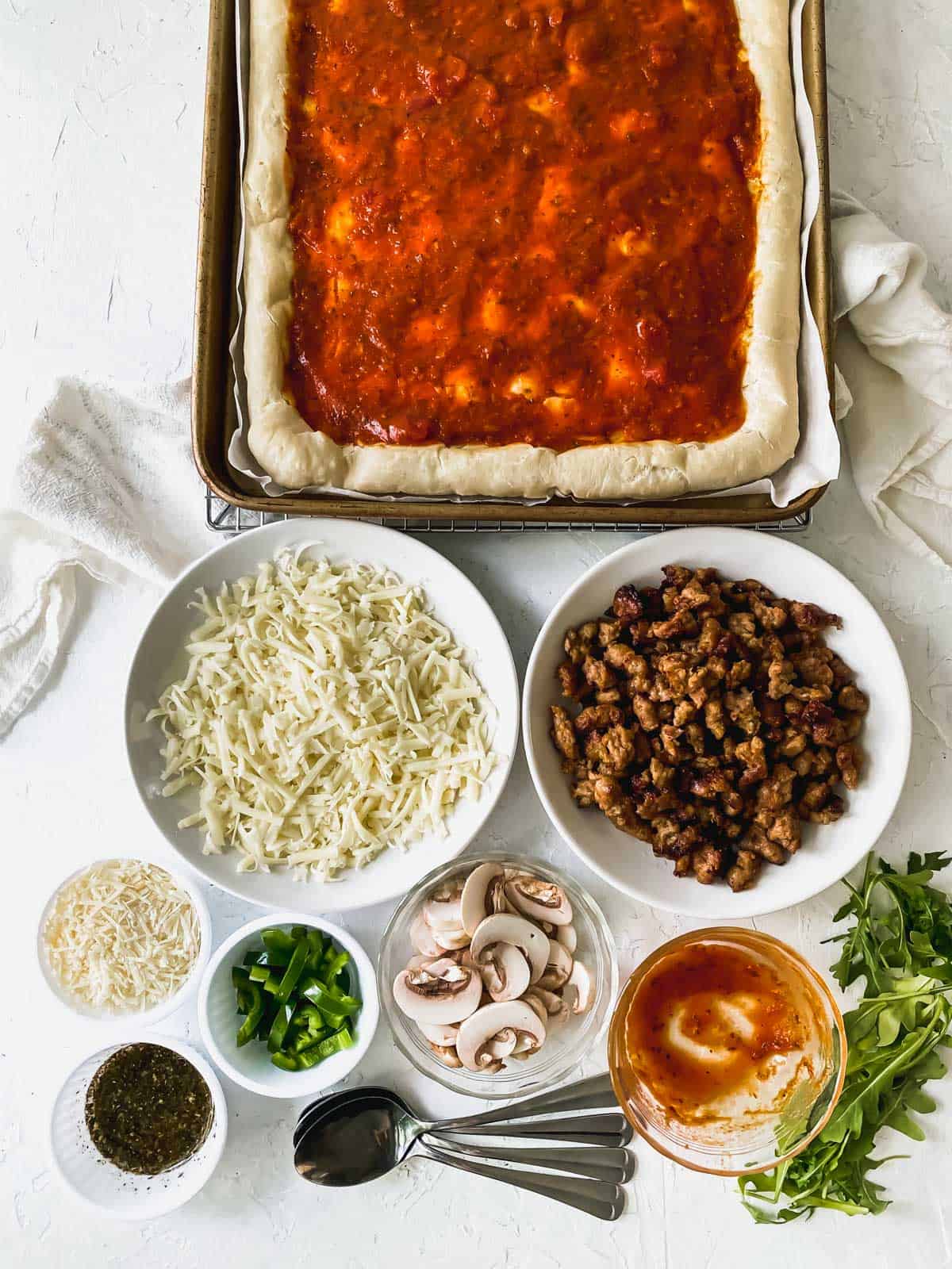 tomato sauce on top of the pizza dough with the rest of the ingredients in small bowls