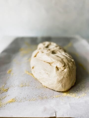 A ball of pizza dough on a baking pan with parchment paper and corn meal