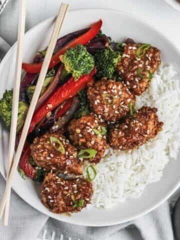 Close up of air fryer almond chicken in honey soy sauce with stir fried veggies, chopsticks, and white rice.