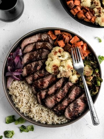 Glazed balsamic steak and veggie bowls with red wine and brussels sprout leaves scattered around it.