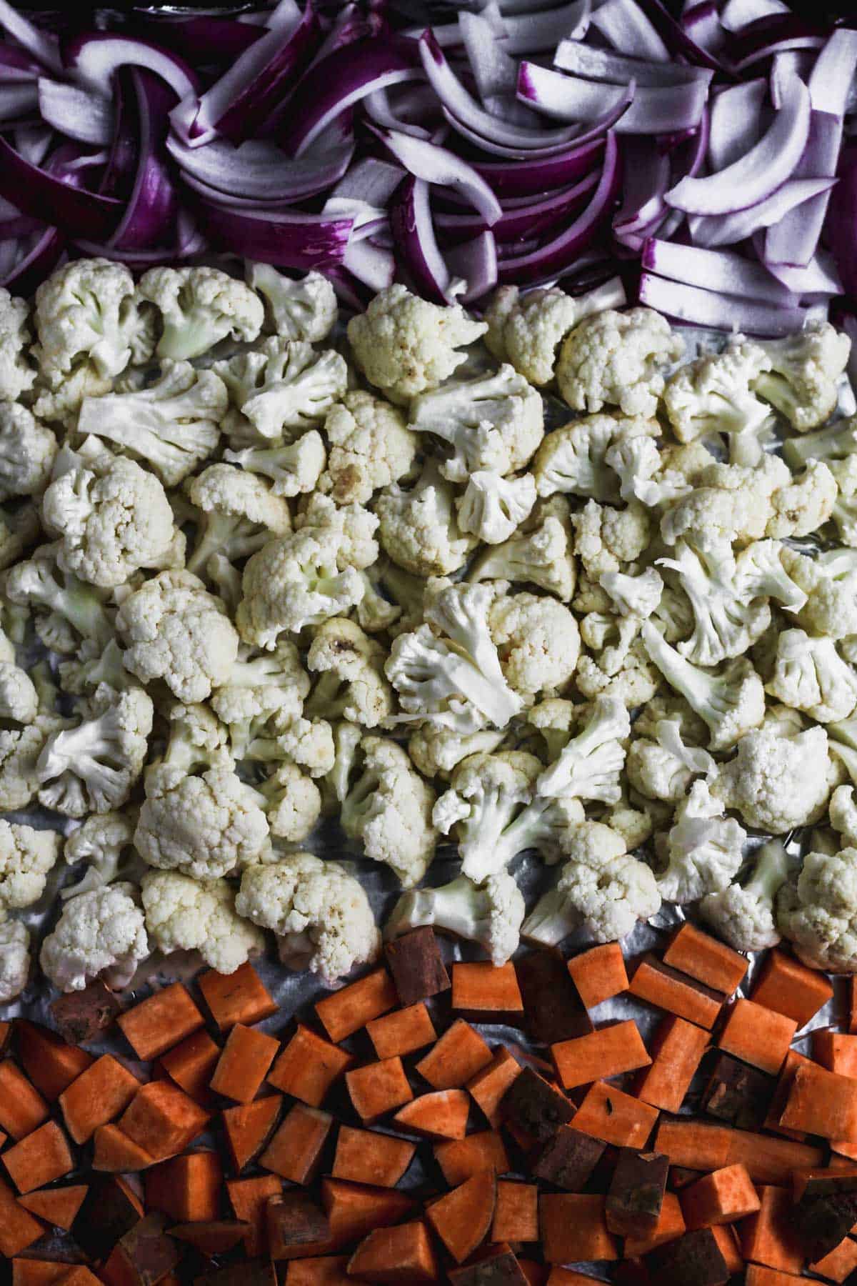 Red onion, cauliflower, and sweet potatoes on a sheet pan.