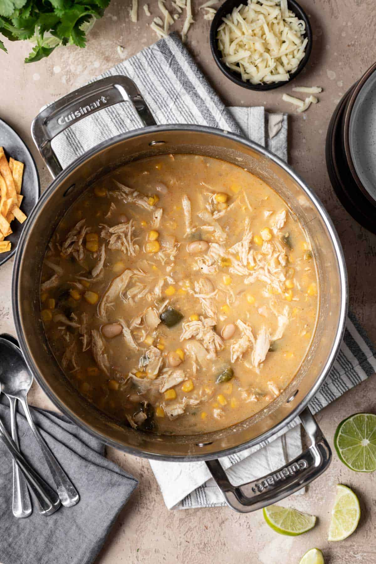 Chicken chili without tomatoes in a large pot with spoons and lime wedges to the side.