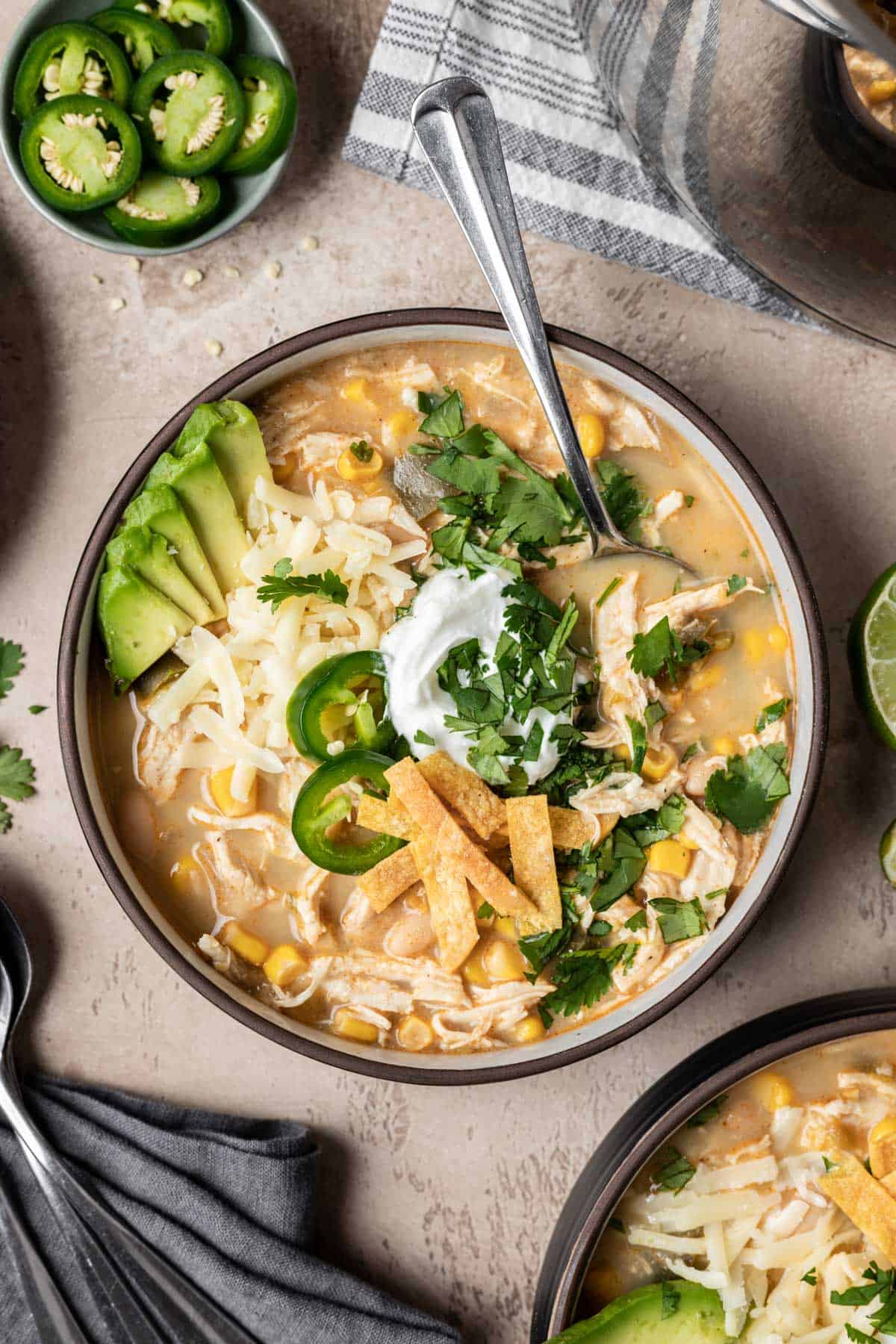 A bowl of chicken chili without tomatoes topped with cilantro, tortilla strips, jalapeño, cheese, and avocado.