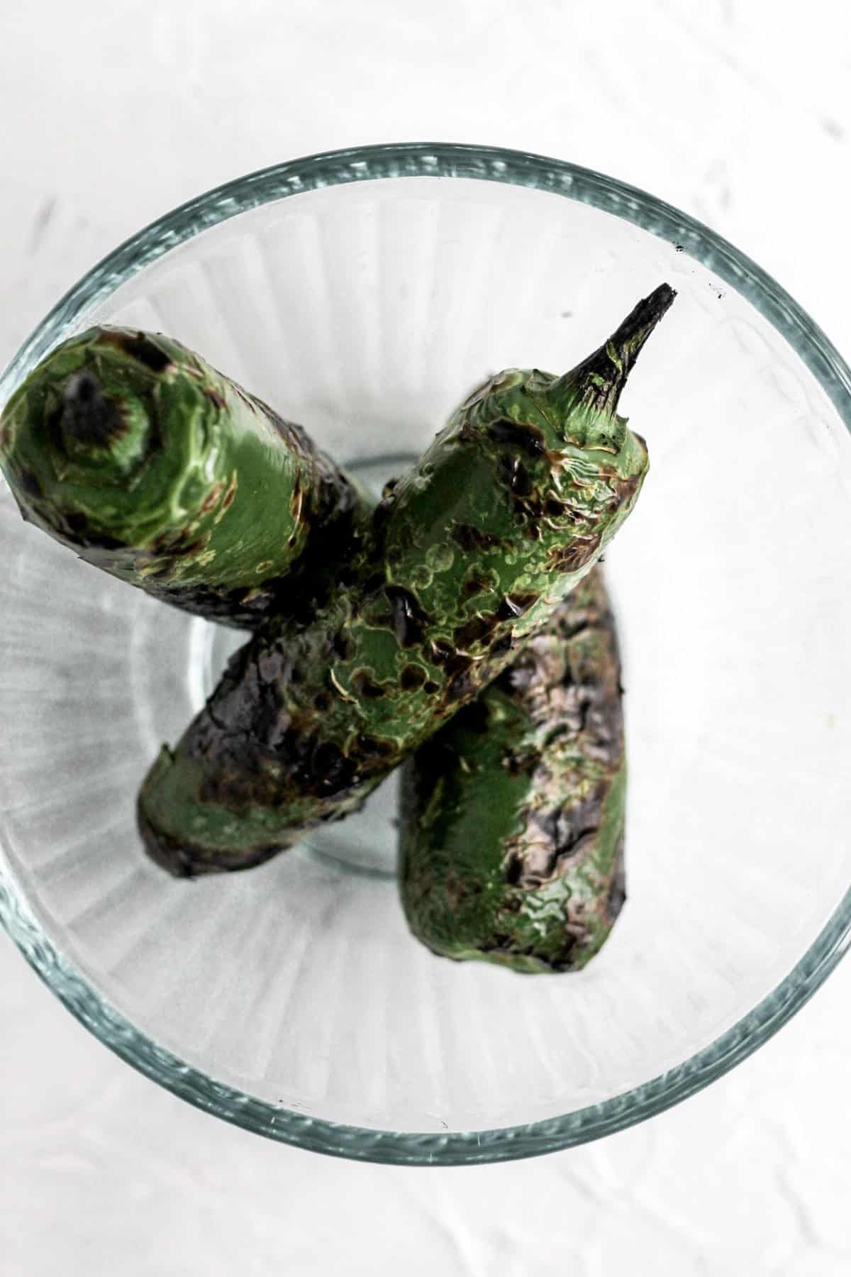 3 charred jalapeños in a glass bowl.