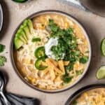 A bowl of chicken chili without tomatoes topped with cilantro, tortilla strips, jalapeño, cheese, and avocado.