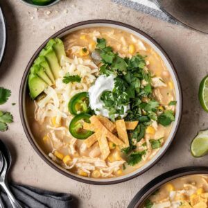 A bowl of chicken chili without tomatoes topped with cilantro, tortilla strips, jalapeño, cheese, and avocado.