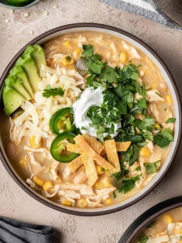 A bowl of chicken chili without tomatoes topped with cilantro, tortilla strips, jalapeño, cheese, and avocado.