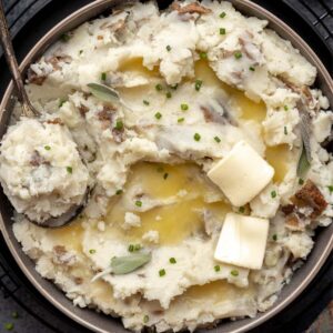 Fluffy almond milk mashed potatoes in a serving bowl topped with butter and a serving spoon.