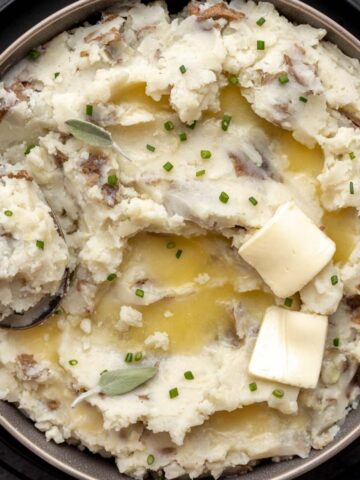 Fluffy almond milk mashed potatoes in a serving bowl topped with butter and a serving spoon.