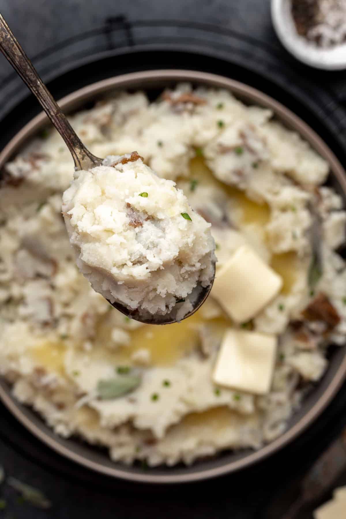 A spoonful of fluffy mashed potatoes over a serving bowl filled with potatoes and melted butter..