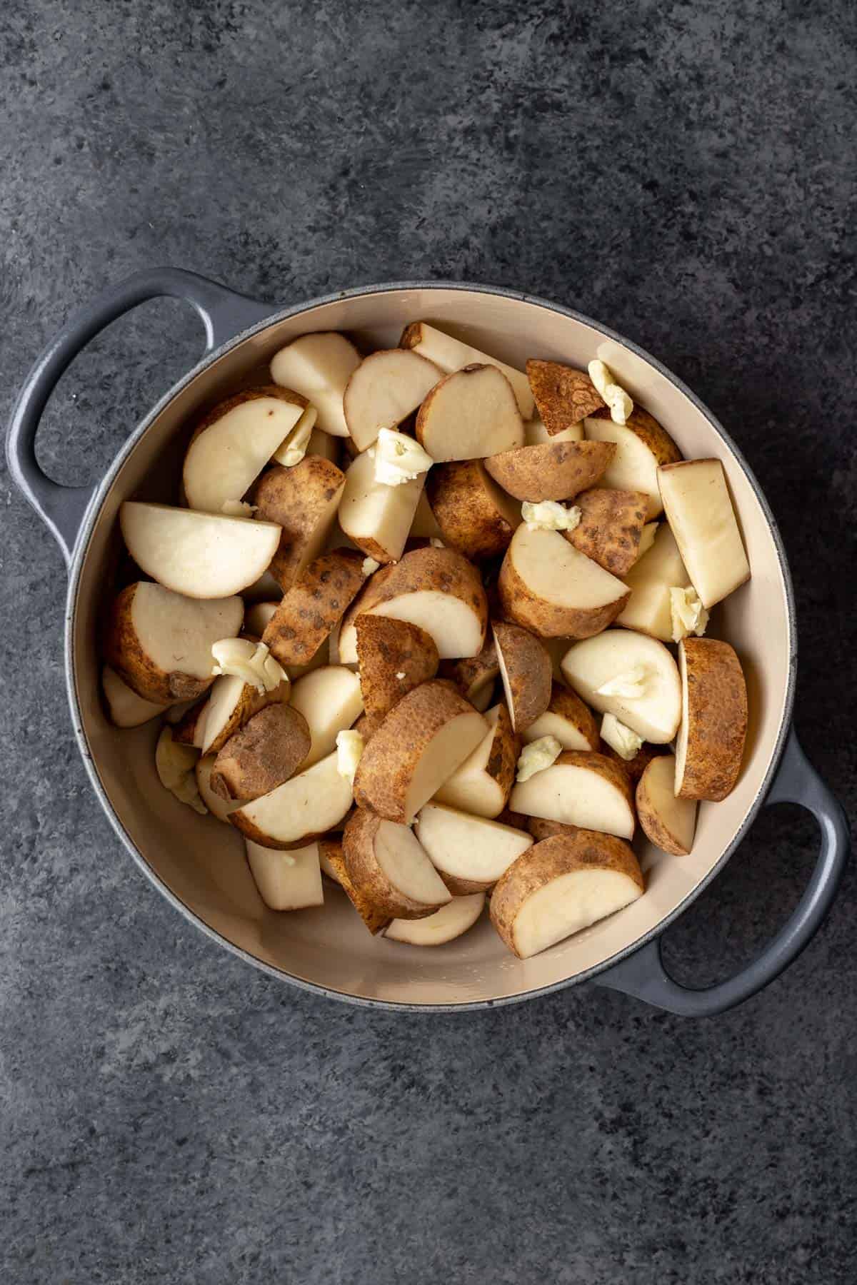Chopped potatoes in a large pot with smashed cloves of garlic.