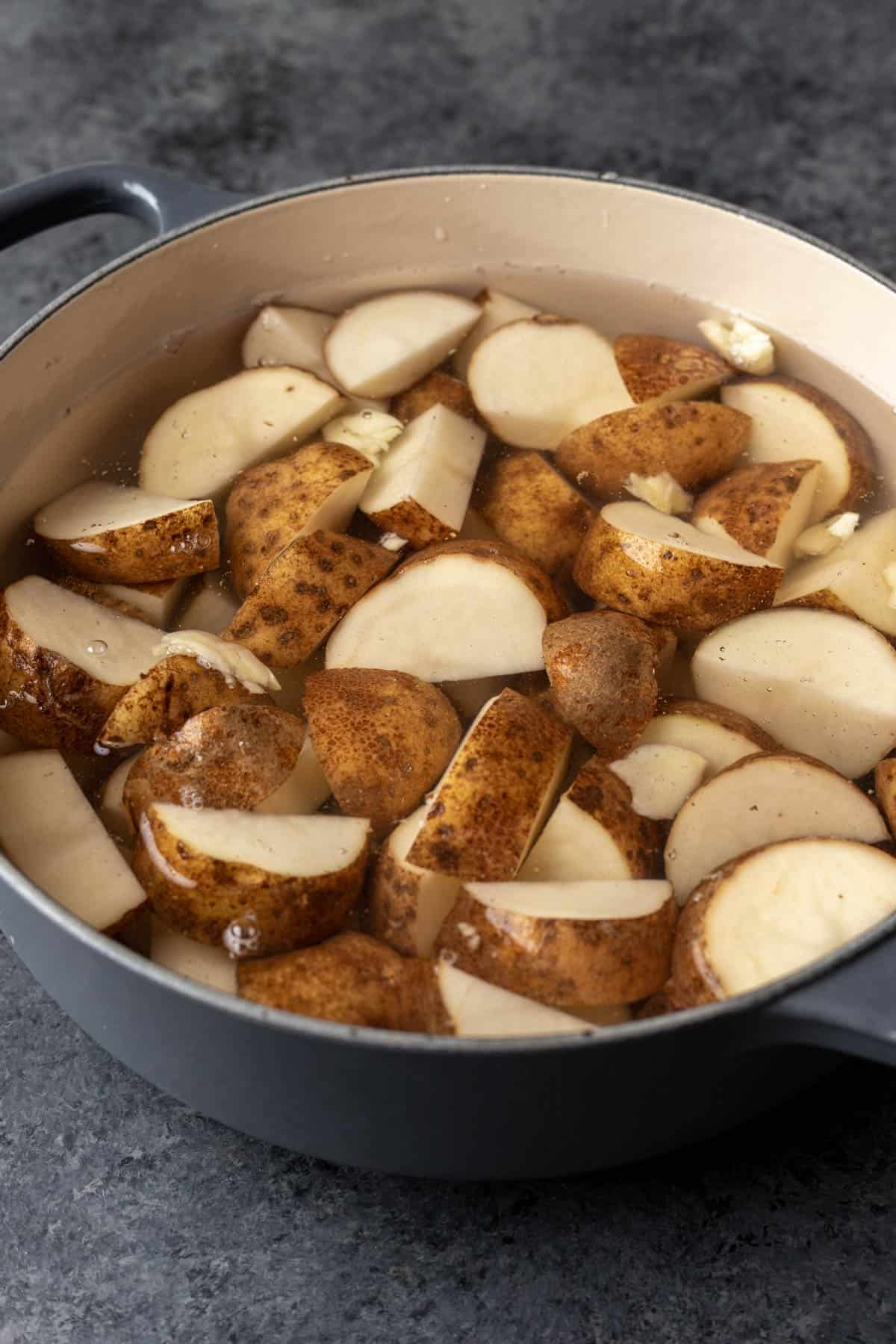 Potatoes and garlic covered with water in a large pot.